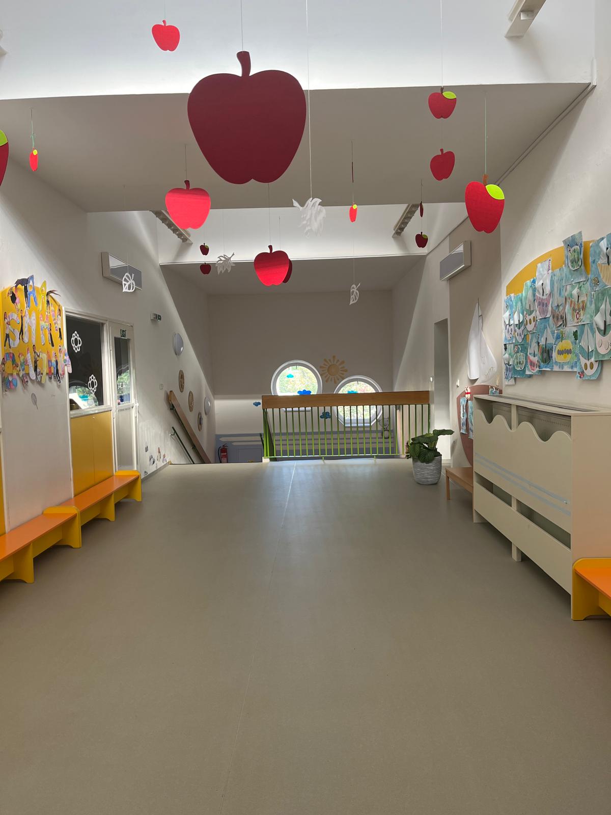 Světlá školní chodba se schodištěm a výstavou dětských prací